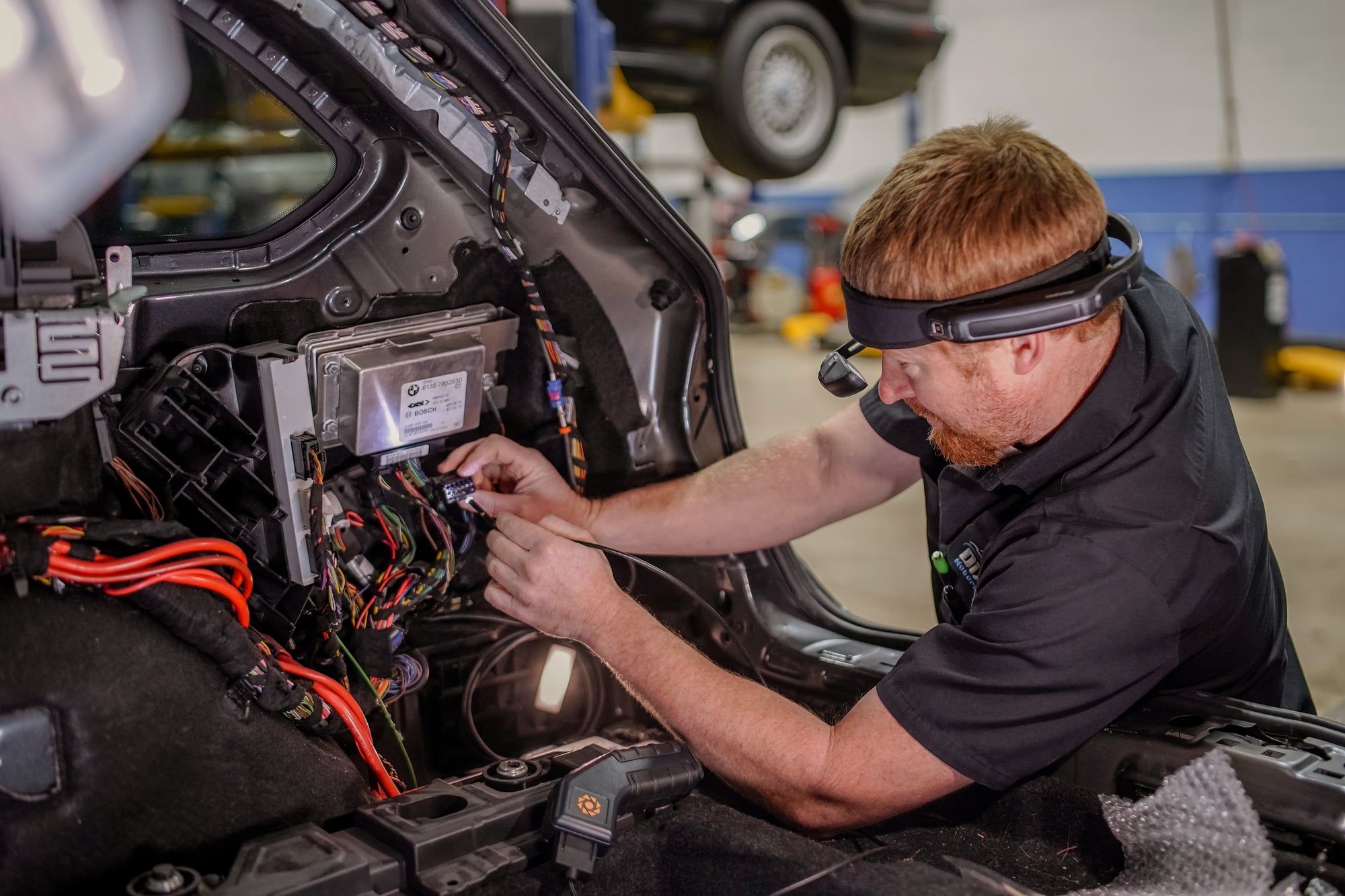 Mechanic working on a car's electrical system in a garage using the RealWear Navigator 520 headset. 