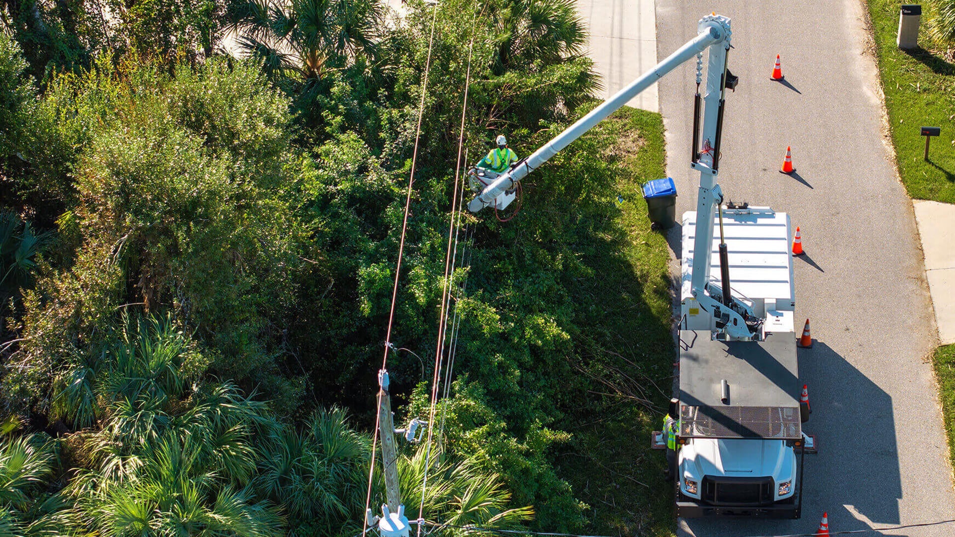 Aerial view of a cherry picker truck working on power lines near trees.